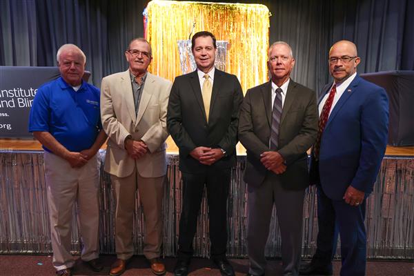 Five men stand shoulder to shoulder and smile at the camera.
